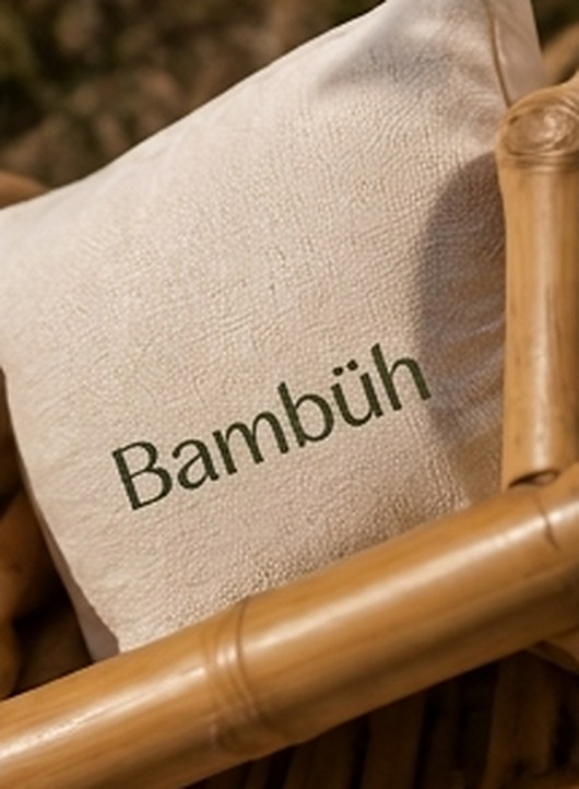 Detalle de cojín de lino con el logotipo de Bambüh sobre un brazo de bambú